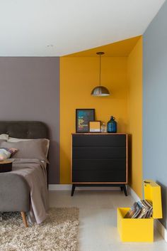 a bedroom with yellow and grey walls, a gray headboard and a black dresser