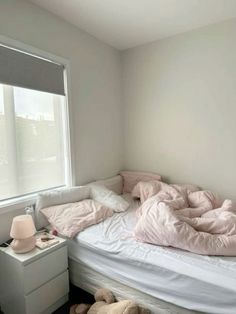 an unmade bed with pink sheets and pillows in a bedroom next to a window