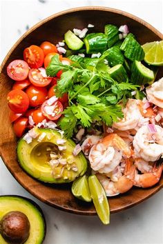 a wooden bowl filled with shrimp, avocado, tomatoes and cilantro