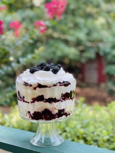 a blueberry cake sitting on top of a green table next to bushes and flowers