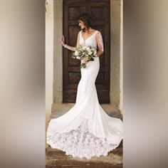 a woman standing in front of a wooden door wearing a white wedding dress and holding a bouquet