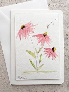 two pink flowers are in front of a white card with a bee on it and one is