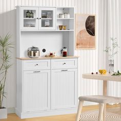 a kitchen with white cupboards and wooden flooring next to a potted plant