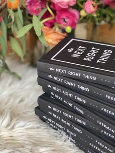 a stack of black books sitting on top of a white rug next to pink flowers