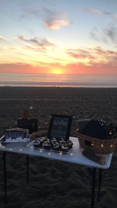 a table with some food on it at the beach in front of the sun setting