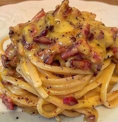 a white plate topped with pasta covered in cheese and bacon on top of it's own