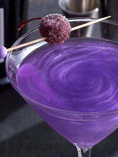 a purple drink in a martini glass with sugar on the rim and a stick sticking out of it