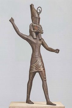 a bronze statue of an egyptian god on a white pedestal with his arms in the air