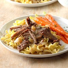 two white plates filled with pasta and meat next to carrots on a wooden table