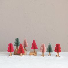 small wooden trees are lined up in front of a gray wall with snow on the ground