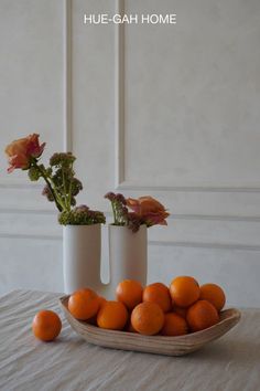 two white vases filled with oranges on top of a table