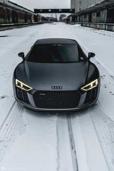 a black sports car parked in the middle of a snowy road next to some buildings