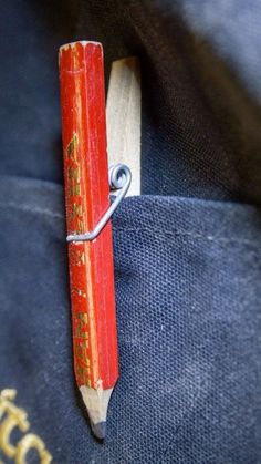 a red pencil with writing on it is tied to a piece of wood that has been placed in the pocket of a backpack