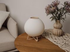 a white vase sitting on top of a wooden table next to a chair and pillow