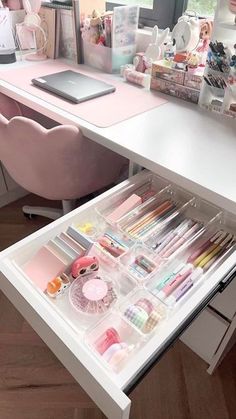 an organized drawer in the middle of a white desk with pink chairs and other items on it