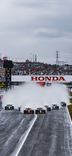 a group of cars driving down a race track in front of a large honda sign