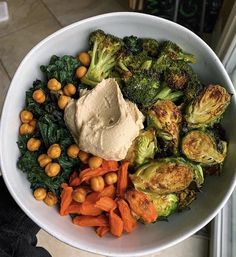 a bowl filled with broccoli, carrots and chickpeas next to some kind of hummus