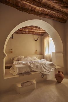 a bed sitting under a window next to a white wall and wooden beams on the ceiling