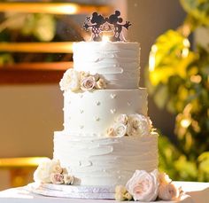 a wedding cake with white frosting and pink flowers on the top is decorated with mickey mouse figurines