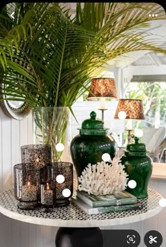 a green vase sitting on top of a table next to candles and a potted plant