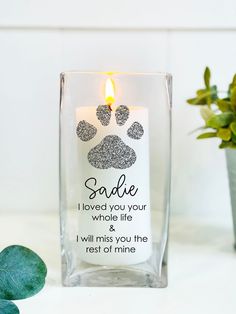 a candle with a paw print on it next to some plants and a potted plant