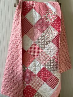 a pink and white quilt hanging from a hook on a door handle with a red and white checkered blanket draped over it