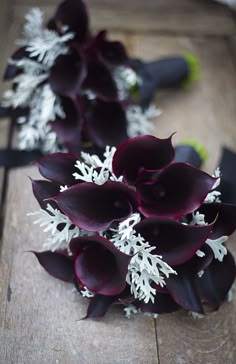 purple and white flowers are arranged on a wooden surface with black ribbon around them,