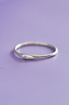 a white gold ring with a diamond on the side, sitting on a purple surface