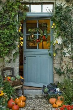 a blue door surrounded by plants and pumpkins in front of an old stone building