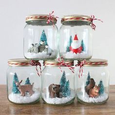 four glass jars with animals in them and snow on the bottom one has a santa hat