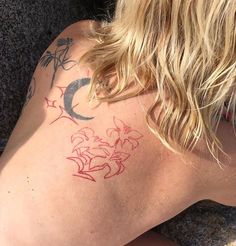 a woman with a tattoo on her back is sitting in the sand and looking down