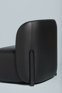 a black leather chair sitting on top of a white floor next to a gray wall