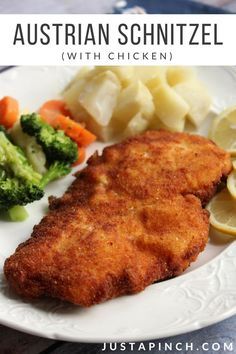 a white plate topped with chicken, potatoes and broccoli next to lemon wedges