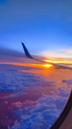 an airplane wing with the sun setting in the distance above clouds and water below it