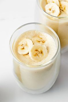 two glasses filled with banana smoothie on top of a white table next to each other