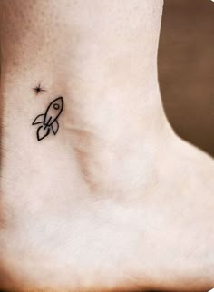 a small tattoo on the ankle of a woman's foot with a rocket ship