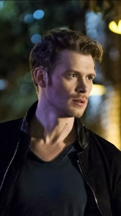 a young man in a black shirt and leather jacket looking off to the side at night