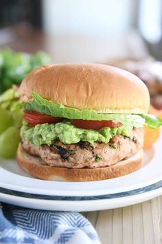 a hamburger with lettuce and tomato on it sitting on a plate next to some pickles