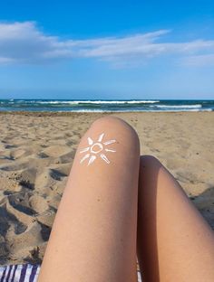 a woman's legs with sun stickers on them sitting in the sand at the beach