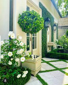 a house with white flowers and bushes in front of the door, on a sunny day