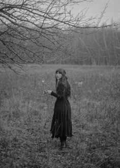 black and white photograph of a woman holding an umbrella in a field with bare trees