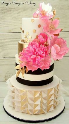 a three tiered cake with pink flowers on the top and gold trimmings