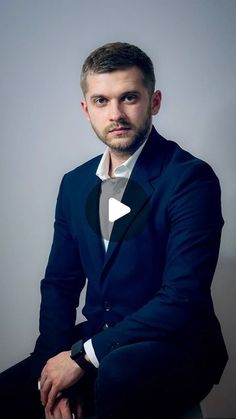 a man in a suit sitting on a chair with his arms crossed and looking at the camera