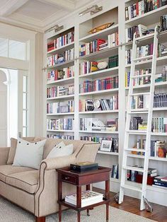 a living room filled with lots of white bookshelves and furniture next to a window