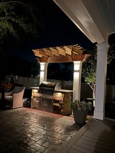 an outdoor bbq grill with lights on at night under a pergolated roof