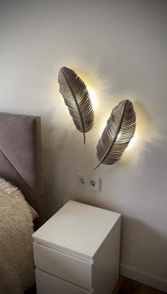 two lights that are on the side of a wall next to a white dresser and bed