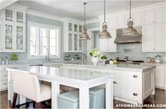 a large kitchen with white cabinets and marble counter tops, two stools at the center island