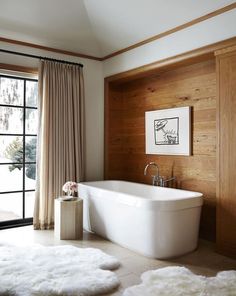 a white bath tub sitting in a bathroom next to a window with wooden paneling