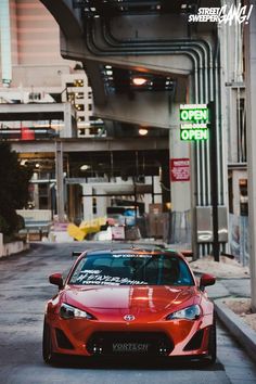 a red sports car parked on the street in front of a building with an open sign above it