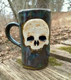 a coffee mug with a skull on it sitting on a wooden table in the woods